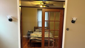 Un dormitorio con una puerta de madera, una cama con colcha a rayas, una mesita de noche y un ventilador de techo.