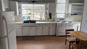 Una cocina con armarios blancos, un lavamanos, una estufa y un ventanal con vistas a árboles.