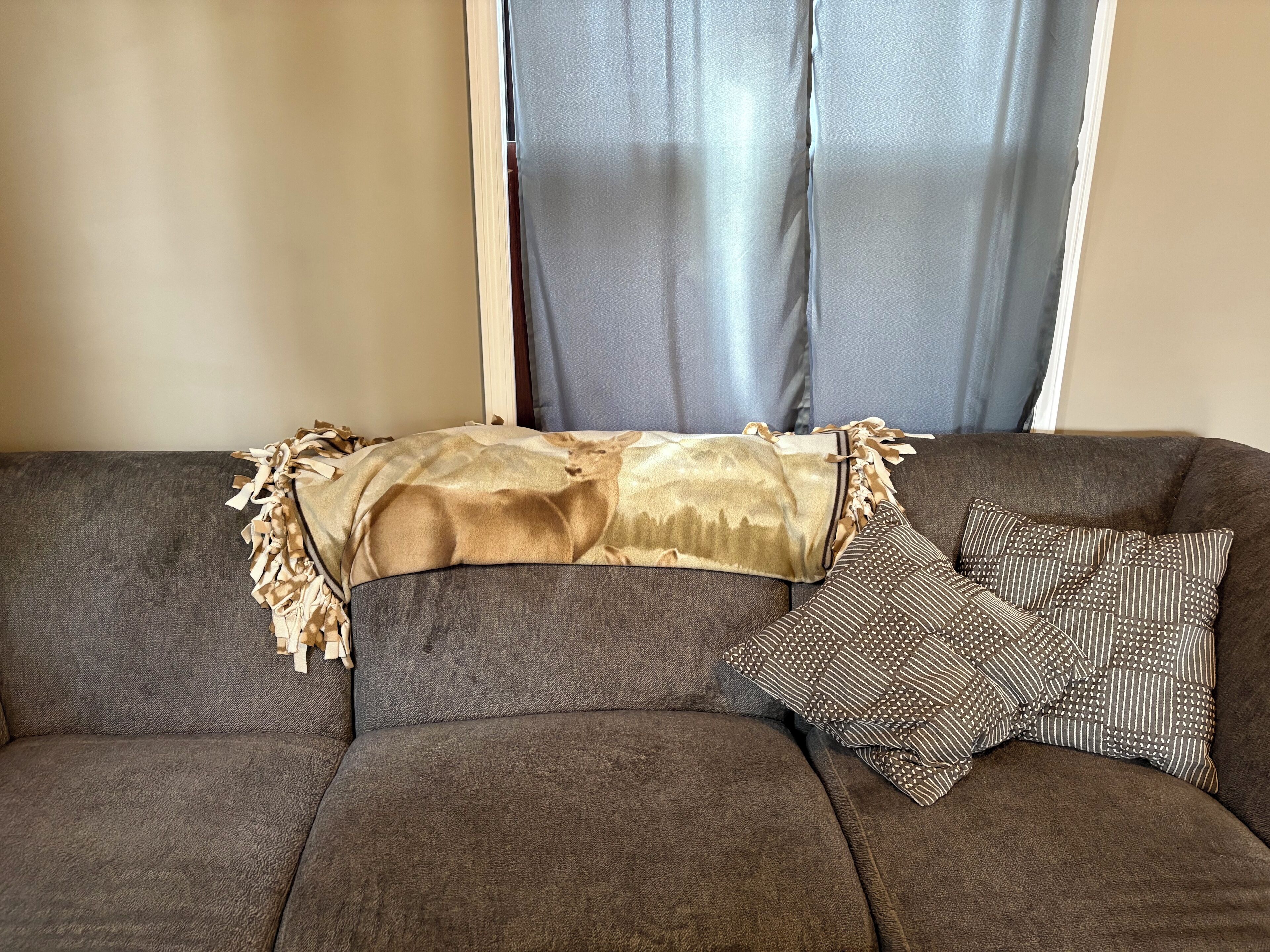 A brown sofa with a patterned pillow and a decorative throw blanket.