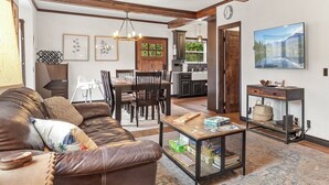 A spacious living room with a brown leather sofa, a coffee table with board games, a dining area with a wooden table and chairs, and a kitchen in the background. - Downtown CDA Retreat – Hot Tub, Deck, & Walk to Lake! (Coeur D Alene)