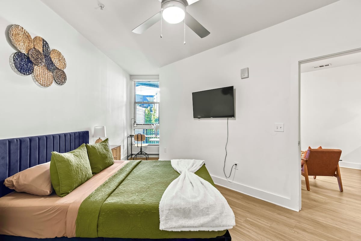 A modern bedroom with a bed, a flat-screen TV, and a ceiling fan.
