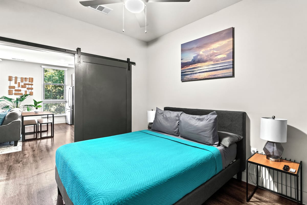 A modern bedroom with a bed, a desk, and a view of the outdoors.