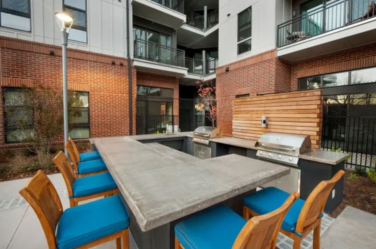 An outdoor kitchen area with a grill, dining table, and chairs.