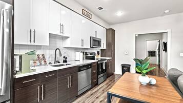A modern kitchen with white and dark wood cabinets, stainless steel appliances, and a wooden dining table with a plant.