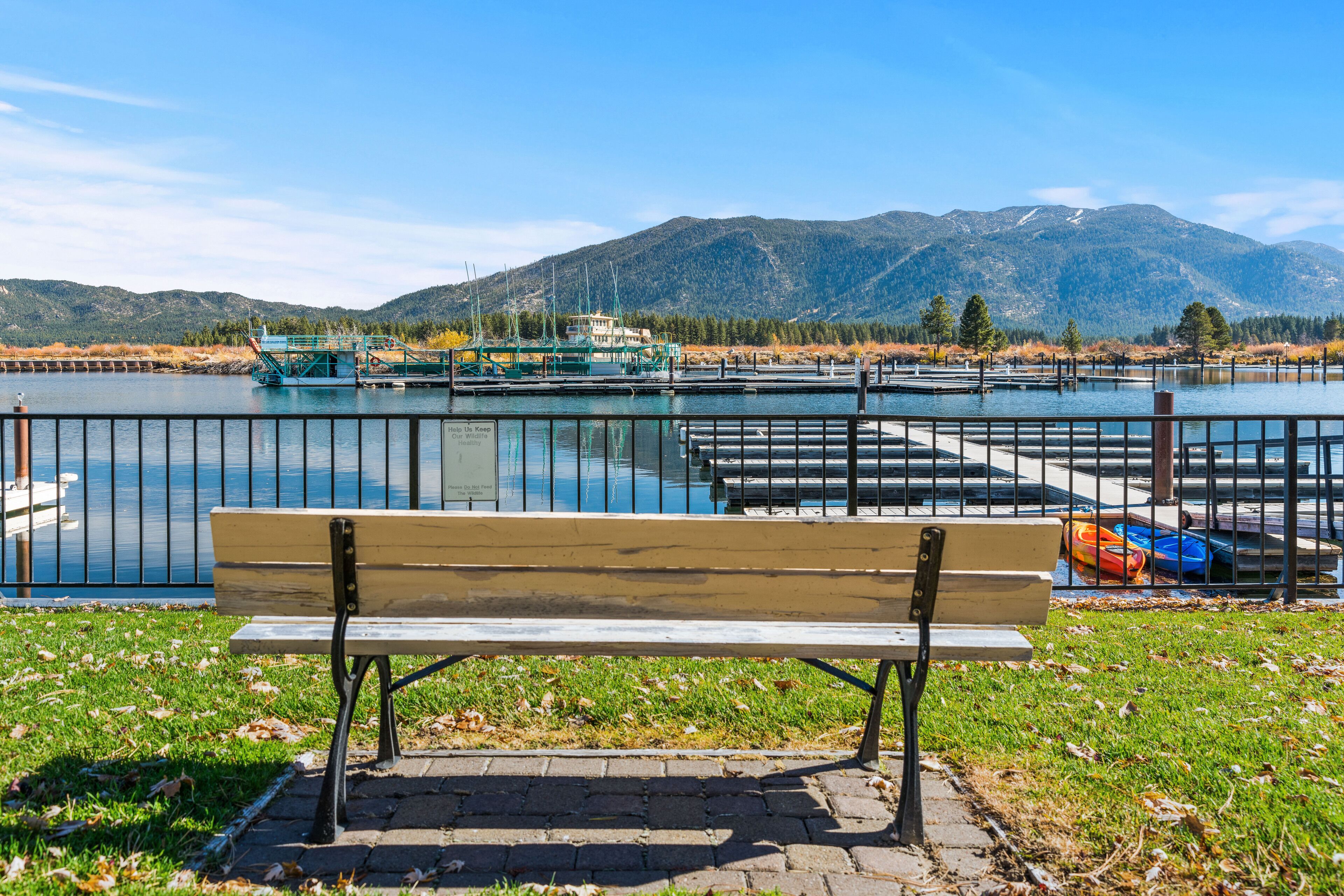 Eine Parkbank mit Blick auf einen See, einen Bootssteg und Berge im Hintergrund.