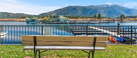 Eine Parkbank mit Blick auf einen See, einen Bootssteg und Berge im Hintergrund.