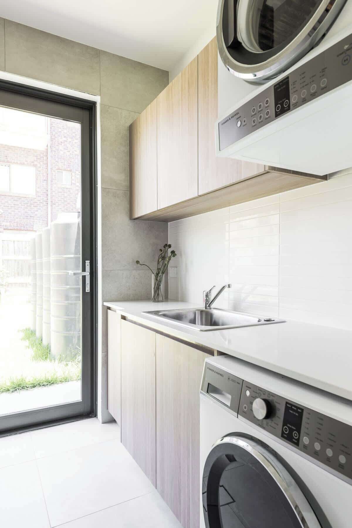 A modern kitchen with a built-in washer and dryer, a sink, and a sliding glass door leading to an outdoor area.