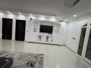 Ein modernes Wohnzimmer mit Flachbildfernseher, weißen Wänden und Fliesenboden.