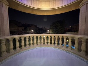 Ein Balkon mit gebogener Brüstung, Fliesenboden und Blick auf den Nachthimmel sowie entfernte Gebäude.