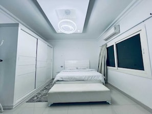 Ein Schlafzimmer mit Bett, Kleiderschrank, Fenster und Deckenleuchte.