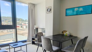 A modern room with a large window, a dining table with four chairs, a small side table, and a painting on the wall. - CBD Gem | Cooling Summer & City View (Wellington)