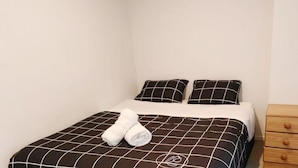 A neatly made bed with a checkered bedspread and two pillows, a wooden nightstand with drawers, and a white wall. - CBD Gem | Cooling Summer & City View (Wellington)