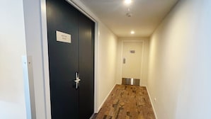 A hallway with a black door labeled "MEETING ROOM," a green emergency exit sign, and a white wall. - CBD Gem | Cooling Summer & City View (Wellington)