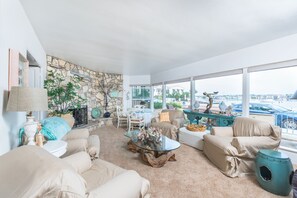 A spacious living room with a stone wall, large windows, and a view of the marina. - 4BR Bayfront Retreat with Stunning Views of Newport Harbor! (Newport Beach)