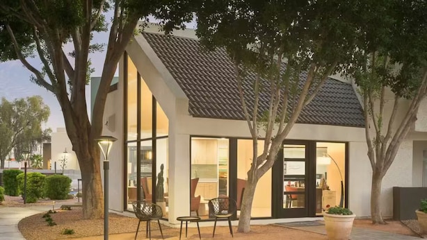 Una casa moderna con amplios ventanales, un patio con sillas y un jardín bien cuidado.