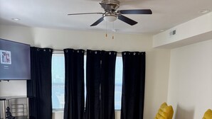 Een moderne woonkamer met een plafondventilator, zwarte en gele stoelen, een witte bank en een televisie aan de muur.