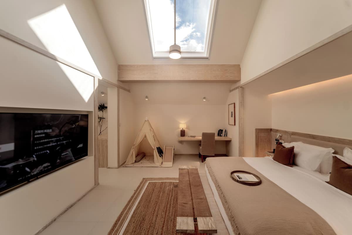 Ett modernt hotellrum med ett takfönster, en säng med ett huvudgavel av trä, ett skrivbord, en stol och en tältliknande konstruktion.