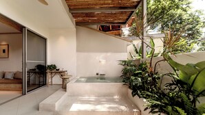 Un escalier extérieur moderne menant à un espace clos par des parois de verre, doté d’un plafond en bois et entouré d’une végétation luxuriante.