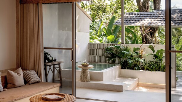 Un intérieur moderne avec un canapé, une petite table et une vue sur une piscine et un jardin, grâce à de grandes portes vitrées.