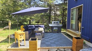 Area patio con barbecue, posti a sedere all'aperto e un ampio ombrellone.