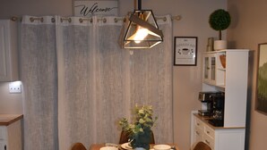 Zona pranzo con tavolo in legno apparecchiato per sei persone, circondato da sedie marroni. Sopra il tavolo, una lampada a sospensione dal design moderno.