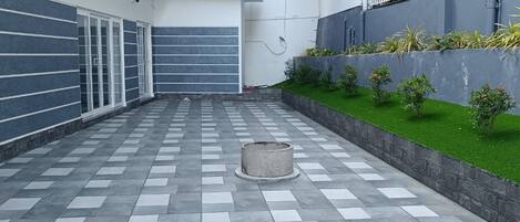 Un cortile con pavimento a scacchi, un piccolo vaso con piante e una struttura metallica a sinistra.