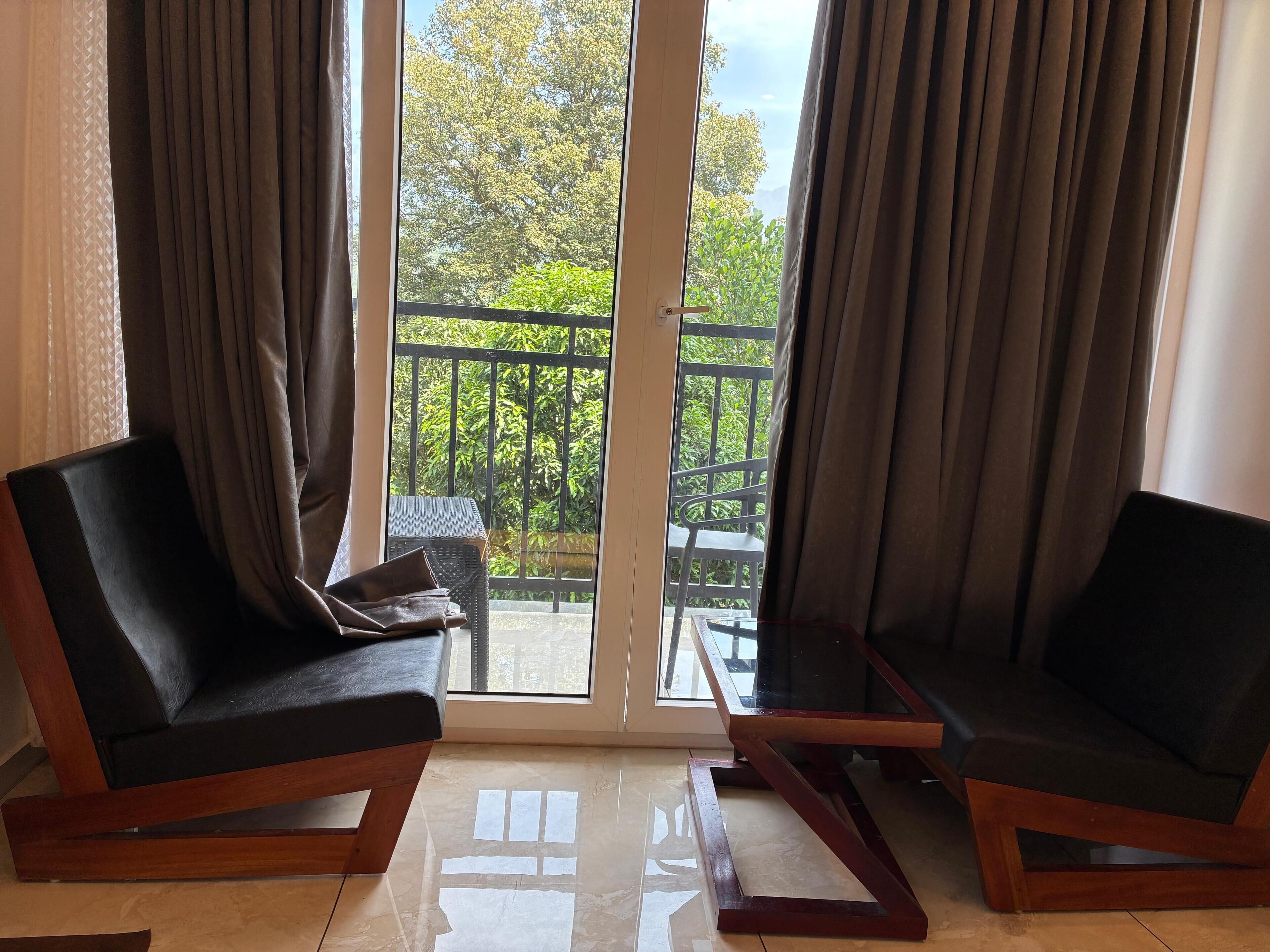 A room with two black sofas, a glass door leading to an outdoor balcony with a metal railing, and a tiled floor.
