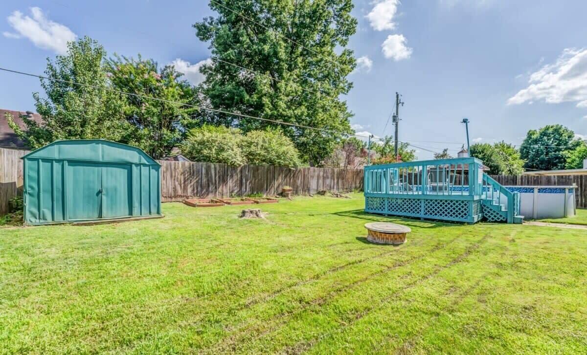 A backyard with a green shed, a blue play structure, and a round table.