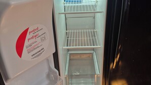 Un refrigerador abierto con un compartimento congelador a la izquierda, una repisa con un recipiente azul y una puerta de vidrio.