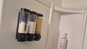Un baño con una puerta blanca, un dispensador de jabón y tres botellas de acondicionador en un soporte de pared.