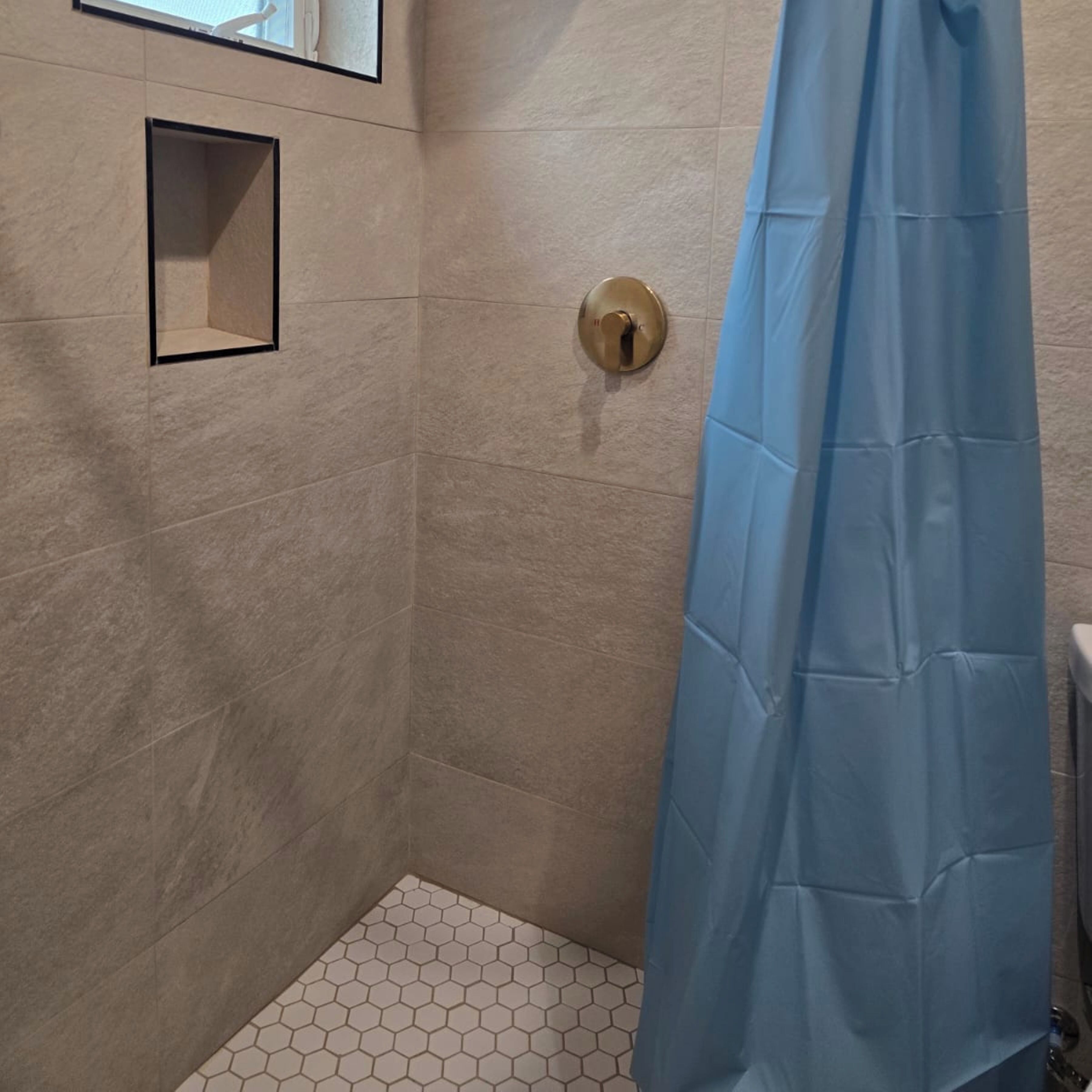 Un espacio de ducha con azulejos color beige, una cortina de ducha azul y un diseño de baldosas hexagonales en el suelo.