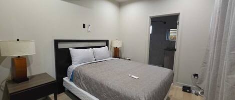 Une chambre d’hôtel bien rangée, avec un lit, des lampes de chevet, une table de nuit, un appareil de climatisation et une porte de salle de bain.