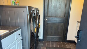 A laundry room with a front-loading washer and dryer, a small countertop, and a door with a doorknob. - The Modern Point- 5 nearby Cedarsports&Cedarpoint (Sandusky)
