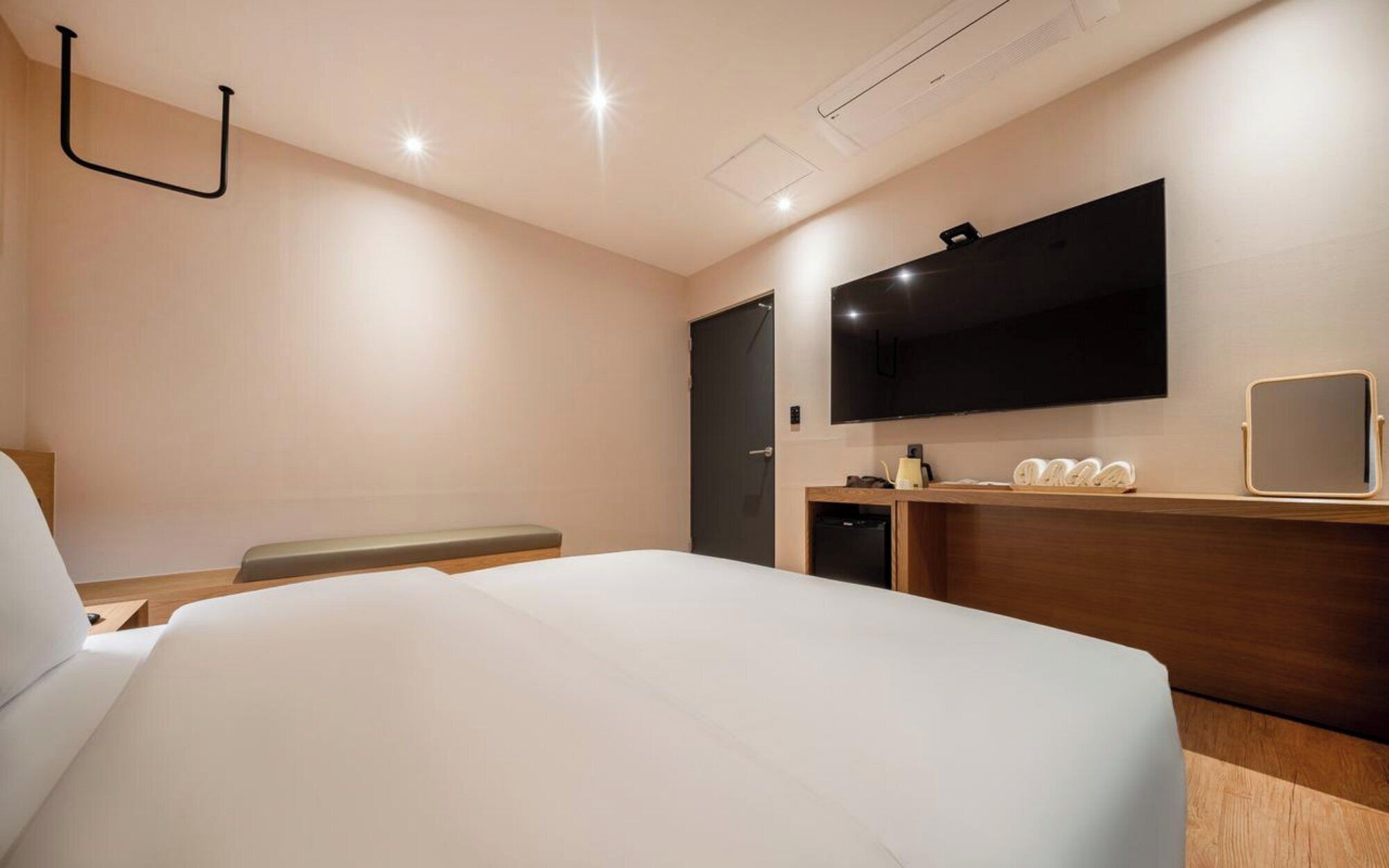 Habitació d'hotel amb un llit, un televisor de pantalla plana penjat a la paret, una taula de nit i un petit mirall.