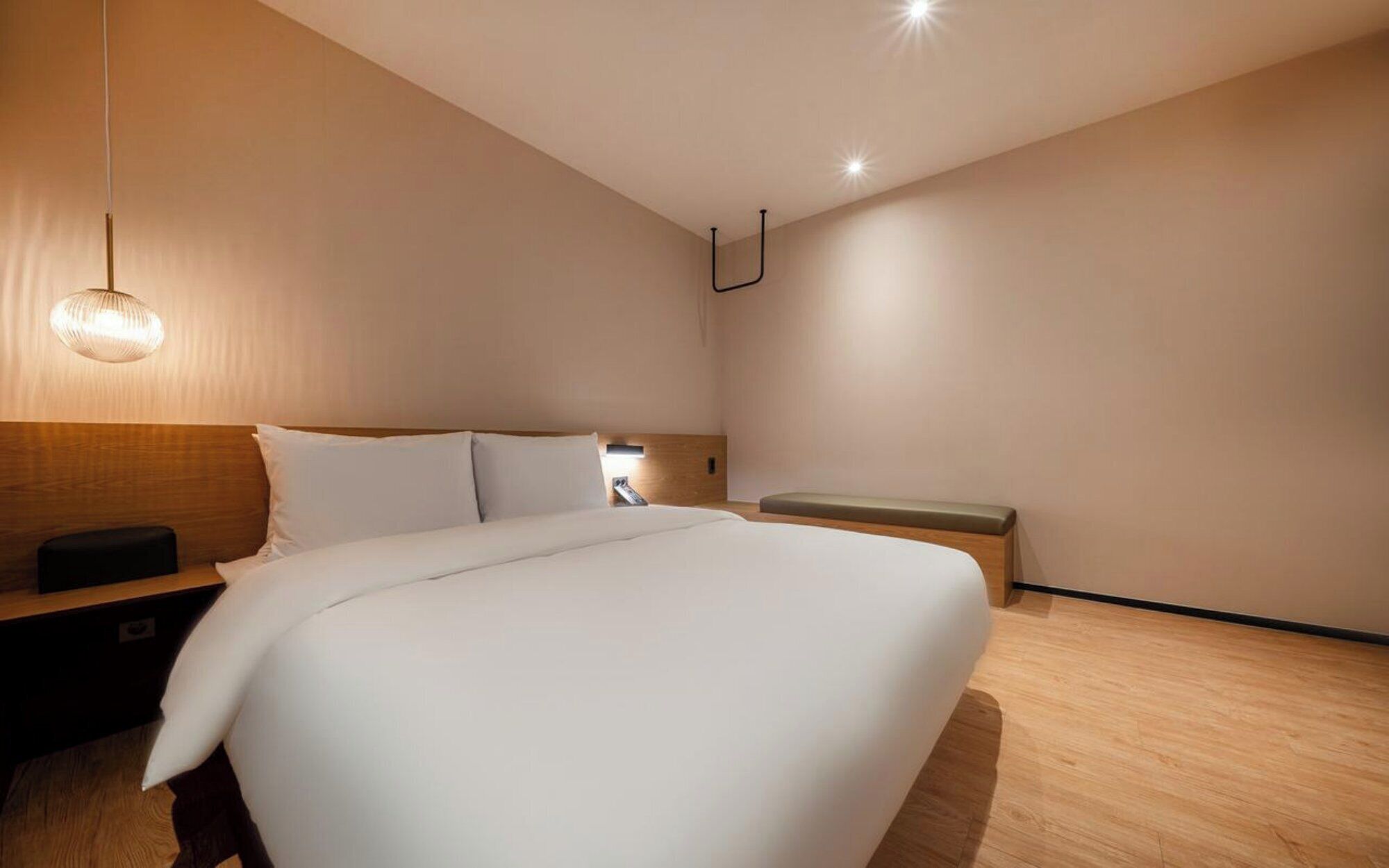 Una habitación de hotel moderna con una cama grande, una mesita de noche, un banco y una lámpara colgante.