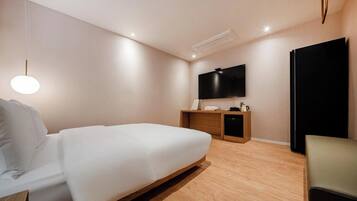 A modern hotel room with a bed, a desk, a TV, and a chair.