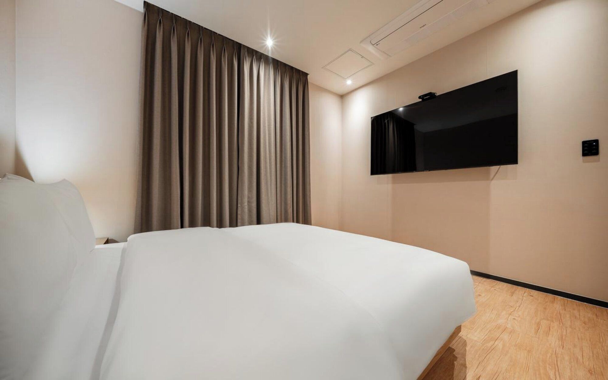 Una habitación de hotel con una cama, un televisor montado en la pared y una cortina.