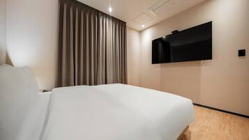 Una habitación de hotel con una cama, un televisor montado en la pared y una cortina.