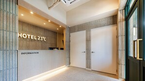 A hotel reception area with a reception desk labeled "HOTEL 23°C" and an "INFORMATION" sign. There are two doors in the background. - HOTEL 23C (Gwangju)