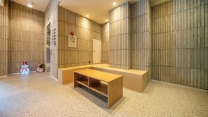 A modern, minimalist bathroom with a wooden bench, a toilet, and a shower area. - HOTEL 23C (Gwangju)