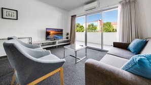 A modern living room with a sofa, two armchairs, a flat-screen TV, and a sliding glass door leading to a balcony. - Spacious 2-bed Conveniently by Lake Tuggeranong (Canberra)