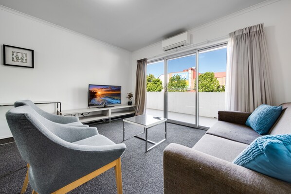 A modern living room with a sofa, two armchairs, a flat-screen TV, and a sliding glass door leading to a balcony. - Spacious 2-bed Conveniently by Lake Tuggeranong (Canberra)