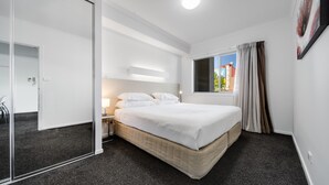 A modern hotel room with a large bed, a bedside table, a mirror, and a window with curtains. - Spacious 2-bed Conveniently by Lake Tuggeranong (Canberra)