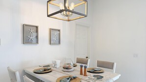 Een eetruimte met een rechthoekige tafel, witte stoelen, een kroonluchter en wanddecoratie van ingelijste zeesterren.