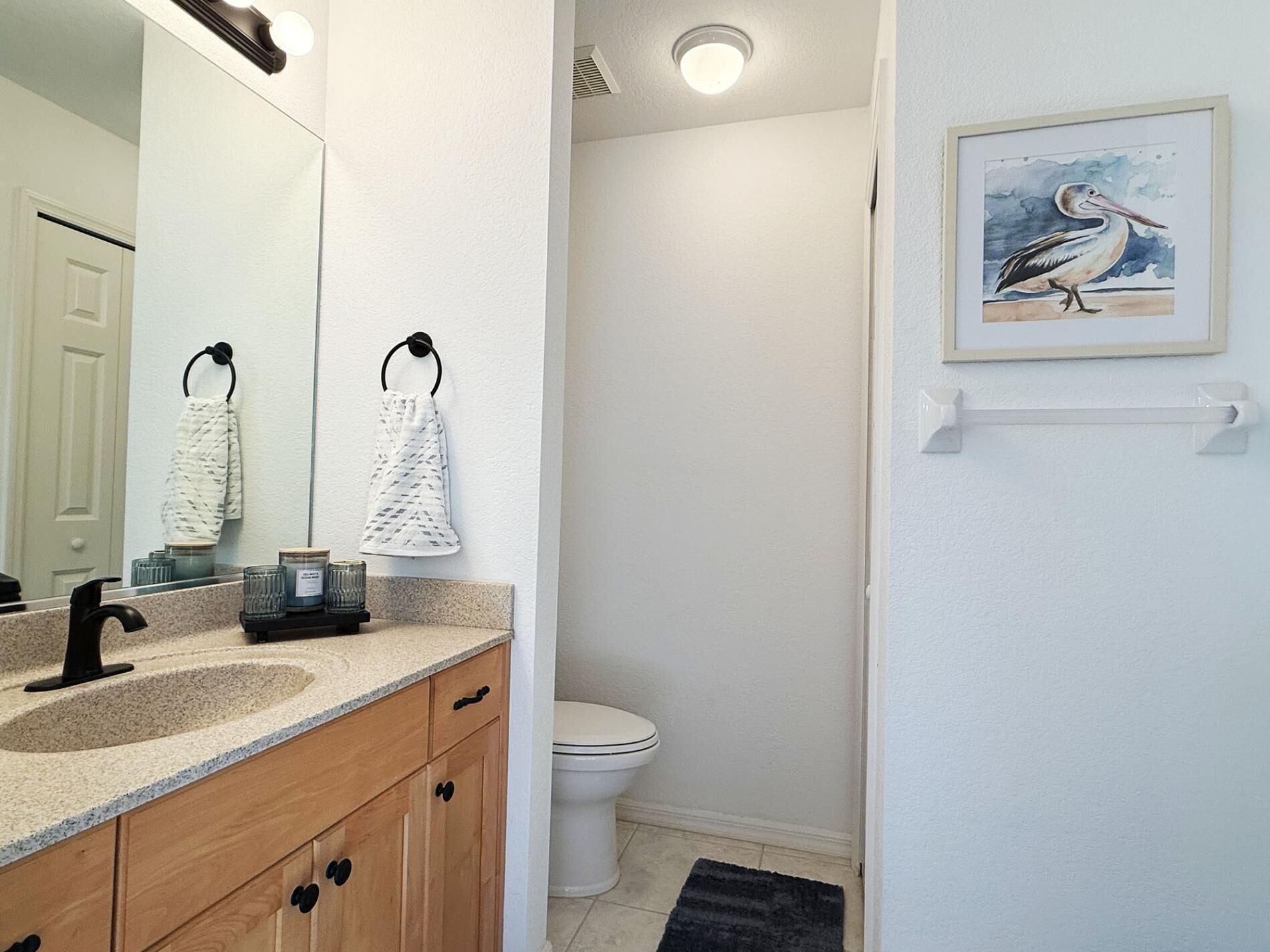 Een badkamer met een wastafel, spiegel, toilet en een kunstwerk met een vogel.