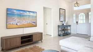 Een ruime woonkamer met een groot strandschilderij, een houten entertainementmeubel en een lichtblauwe console tafel met decoratieve objecten.