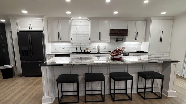 A modern kitchen with white cabinetry, a black refrigerator, and a marble countertop. - GAMEDAY ON 43 (Northport)