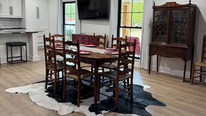 A spacious dining area with a wooden table and chairs, a large flat-screen TV mounted on the wall, and a cabinet with glass doors. - GAMEDAY ON 43 (Northport)