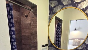 Un baño con ducha, lavamanos con espejo y pared con diseño.