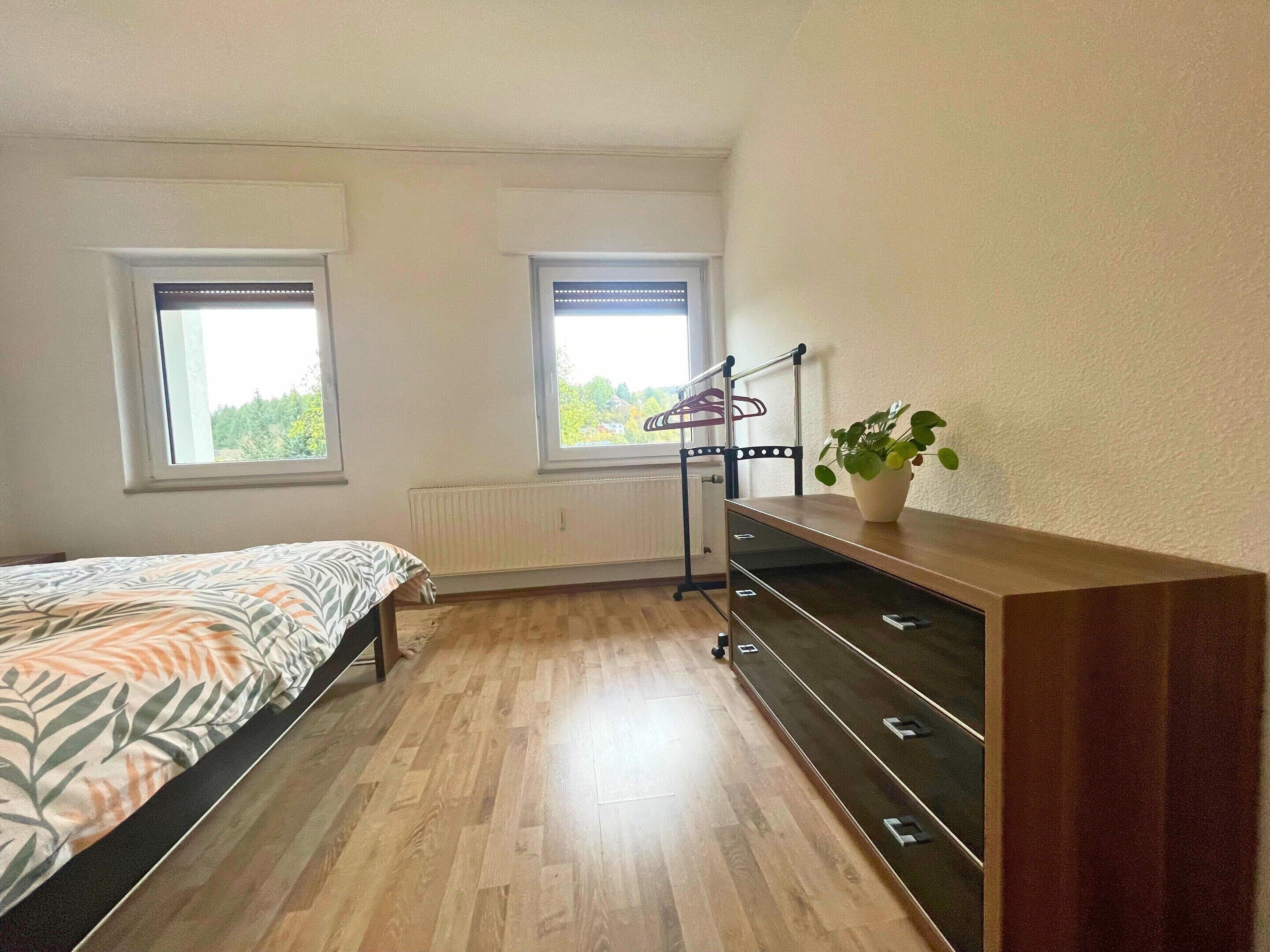 A bedroom with a bed, a dresser, a radiator, and two windows.